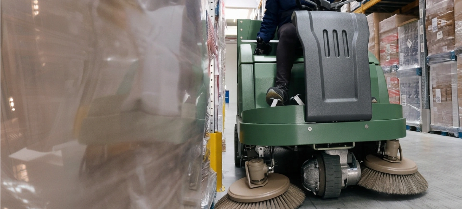 Pulizie industriali: spazzatrice al lavoro tra le scaffalature di un magazzino